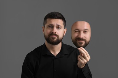 Image of Man holding mask with his facial expression on grey background. Personality crisis, different emotions