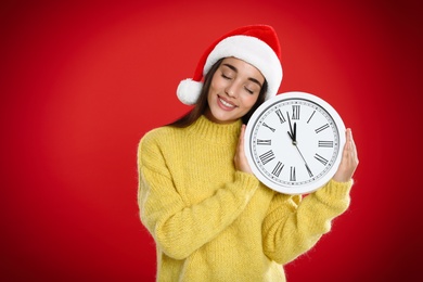 Woman in Santa hat with clock on red background. New Year countdown