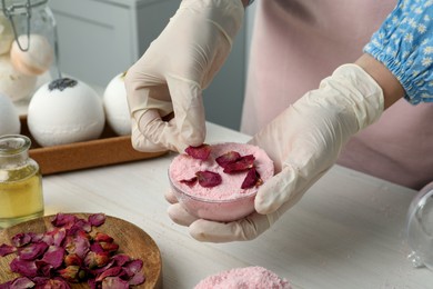 Photo of Woman putting flower petals in bath bomb mold at white table indoors, closeup
