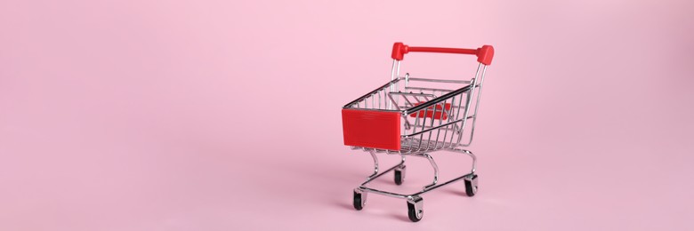 Photo of Small metal shopping cart on pink background, space for text