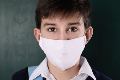 Boy wearing protective mask near chalkboard, closeup. Child safety