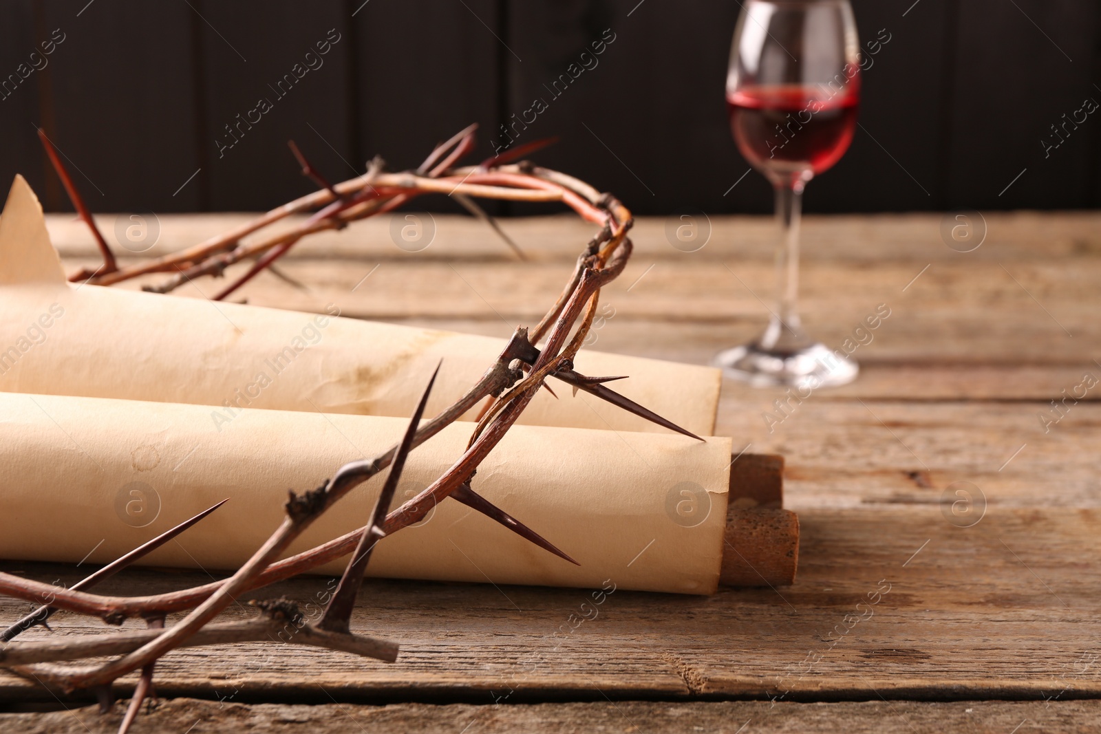 Photo of Crown of thorns, old scrolls and glass with wine on wooden table, selective focus