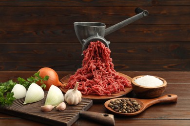 Photo of Meat grinder with beef mince, onion, parsley, garlic and spices on wooden table