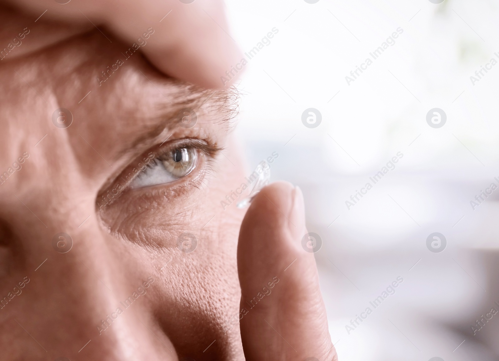 Photo of Mature man putting contact lens in his eye on light background, closeup