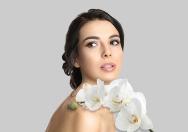 Image of Beautiful young woman and orchid flowers on light background. Spa portrait