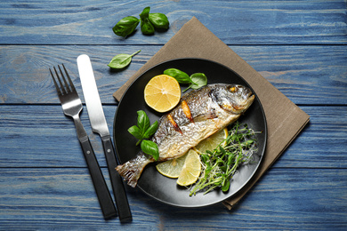 Delicious roasted fish with lemon on blue wooden table, flat lay