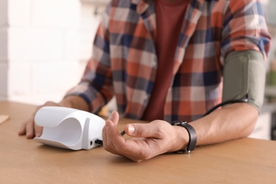 Photo of Man checking blood pressure with sphygmomanometer at table indoors, closeup. Cardiology concept