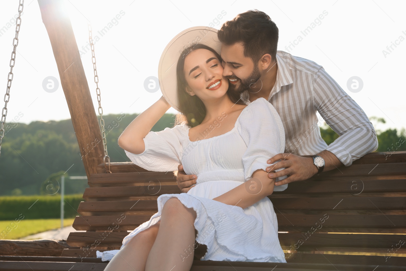 Photo of Romantic date. Beautiful couple spending time together on swing bench outdoors