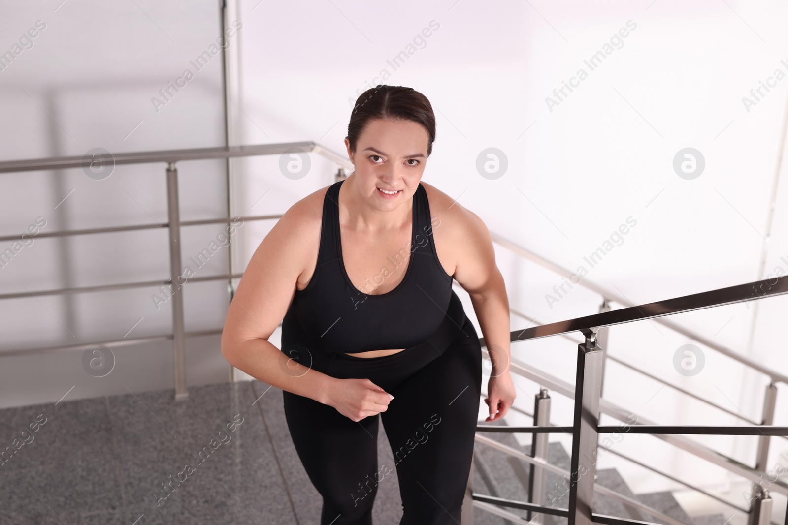 Photo of Overweight woman in sportswear running upstairs indoors