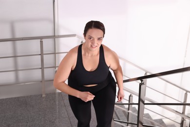 Overweight woman in sportswear running upstairs indoors