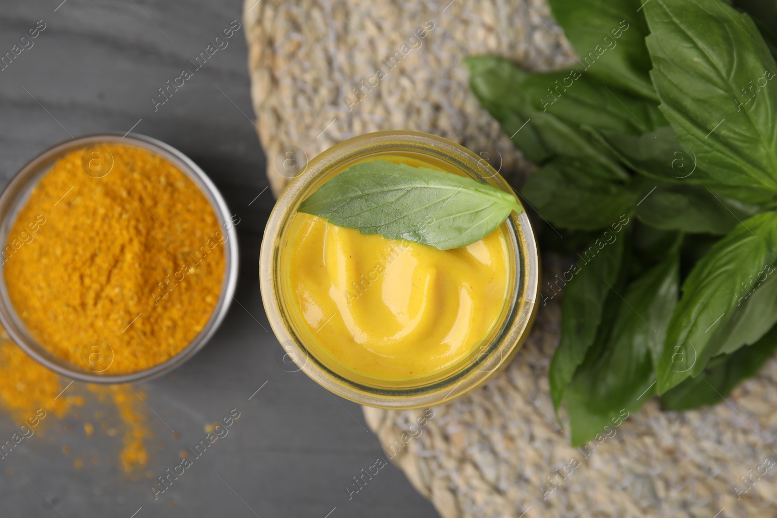 Photo of Tasty curry sauce, powder and basil leaves on grey wooden table, flat lay