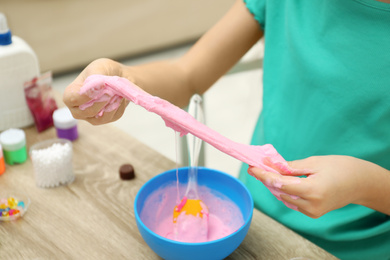 Photo of Little girl making DIY slime toy at table indoors, closeup