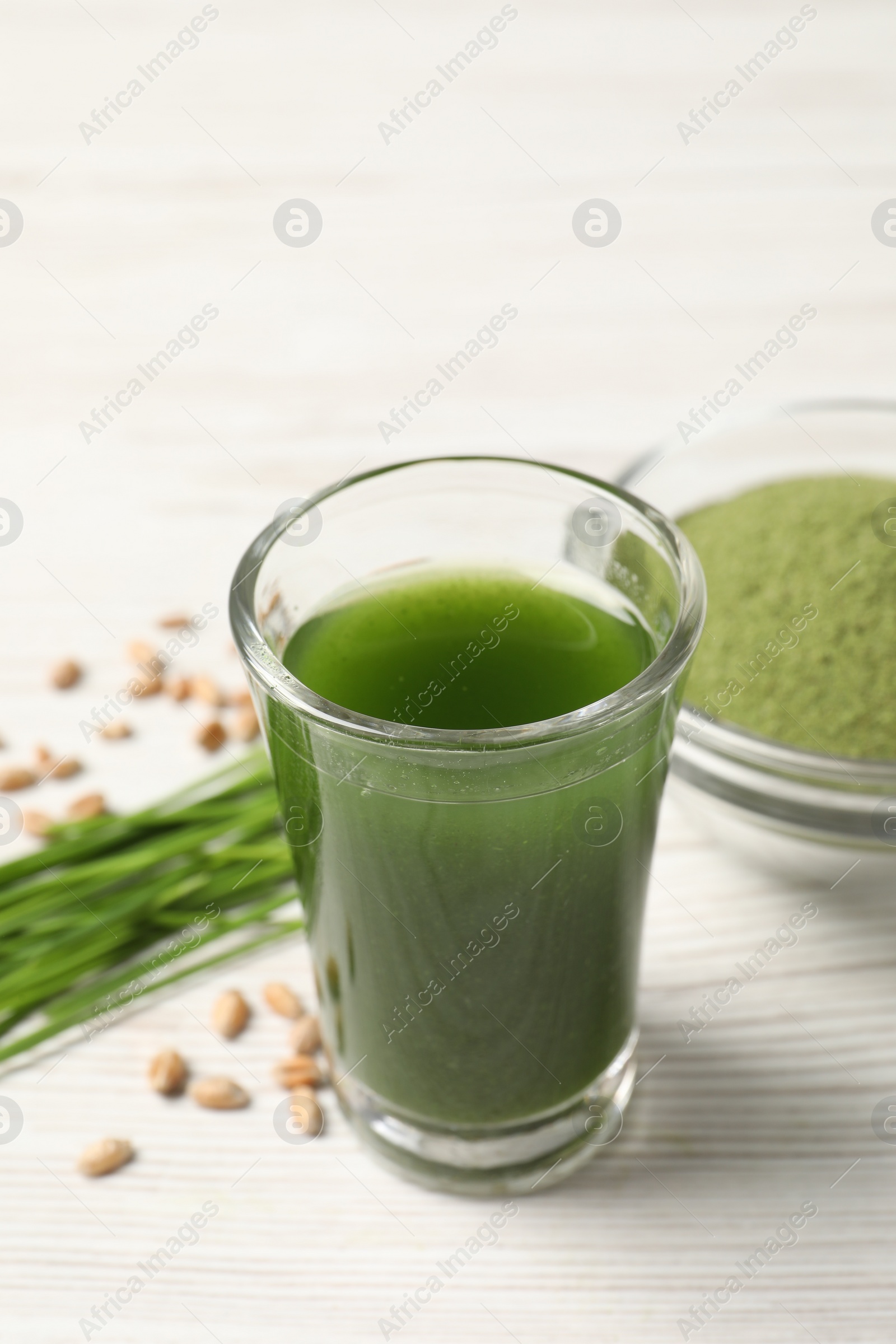 Photo of Wheat grass drink in shot glass on white wooden table, closeup