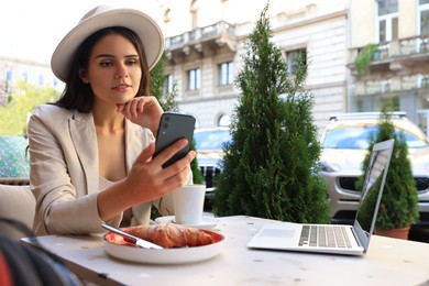 Beautiful young woman using smartphone in outdoor cafe