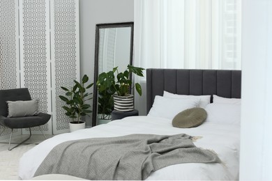 Large comfortable bed and beautiful houseplants in room. Bedroom interior