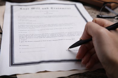 Photo of Woman signing last will and testament at table, closeup