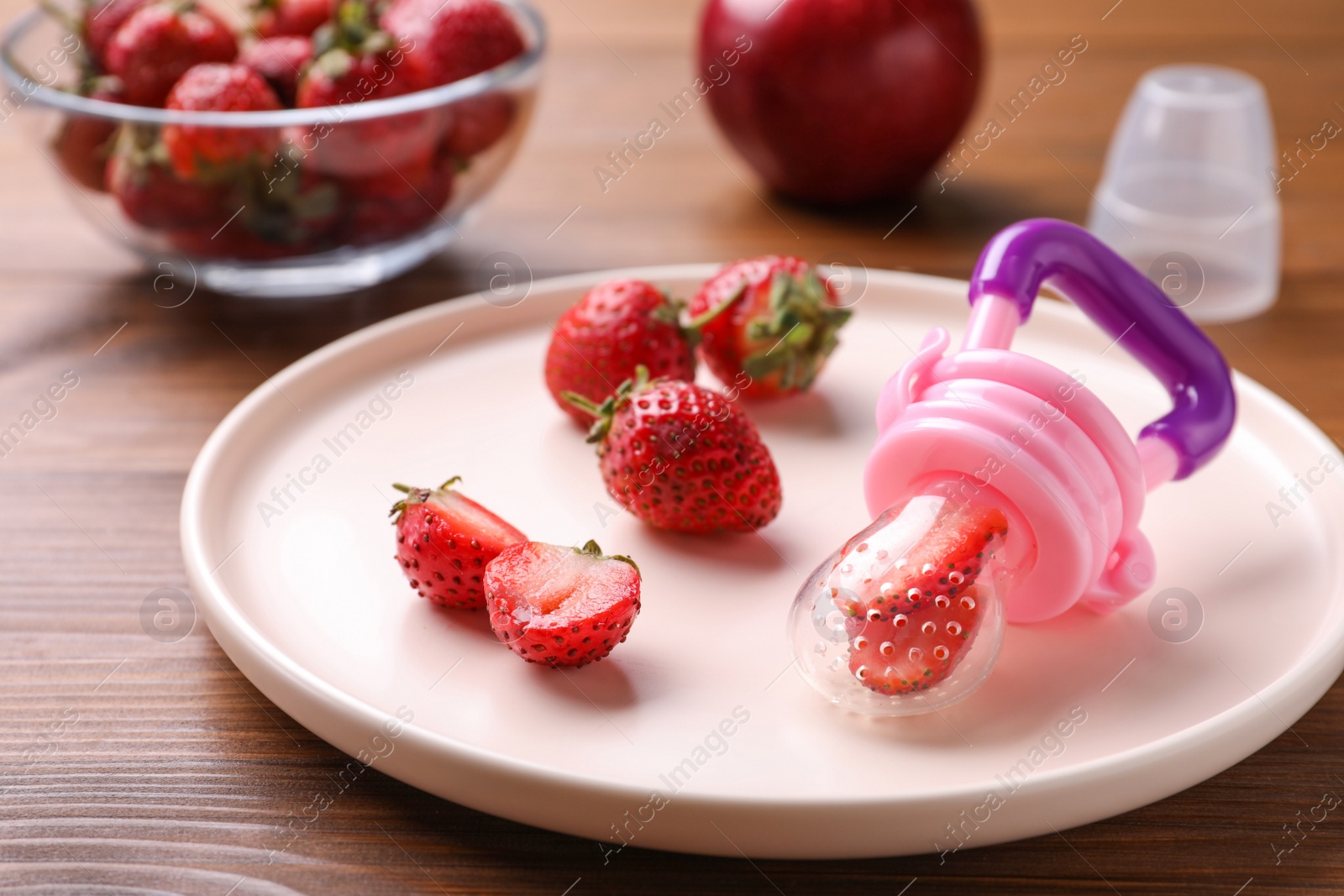 Photo of Nibbler with fresh strawberries on wooden table. Baby feeder