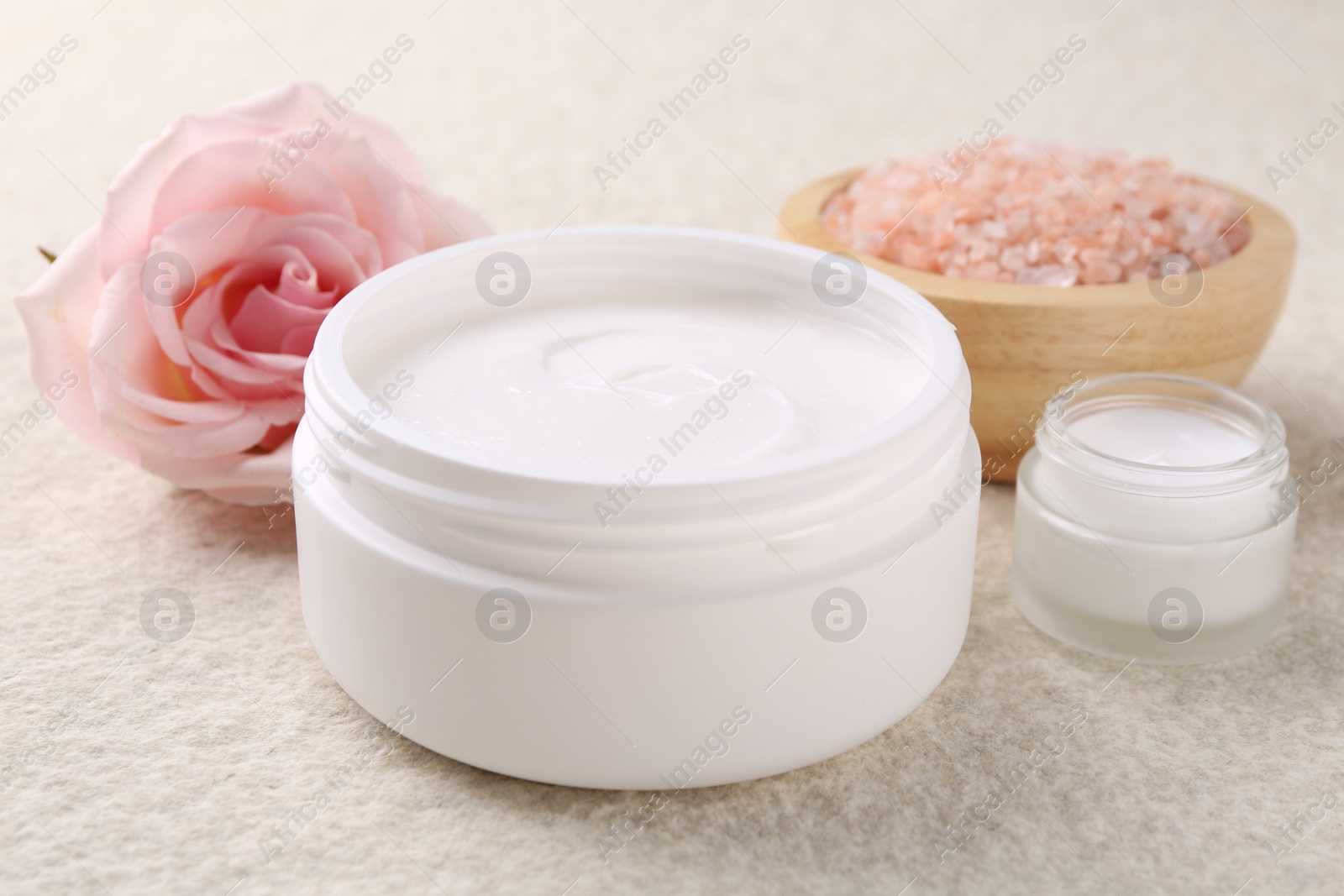 Photo of Composition with body care cream in open jars on light textured table, closeup