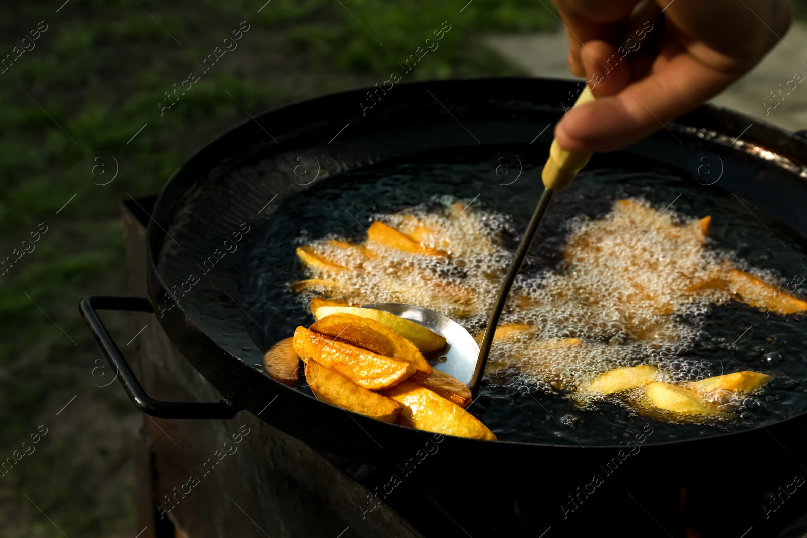 Photo of Man cooking delicious potato wedges on frying pan outdoors, closeup