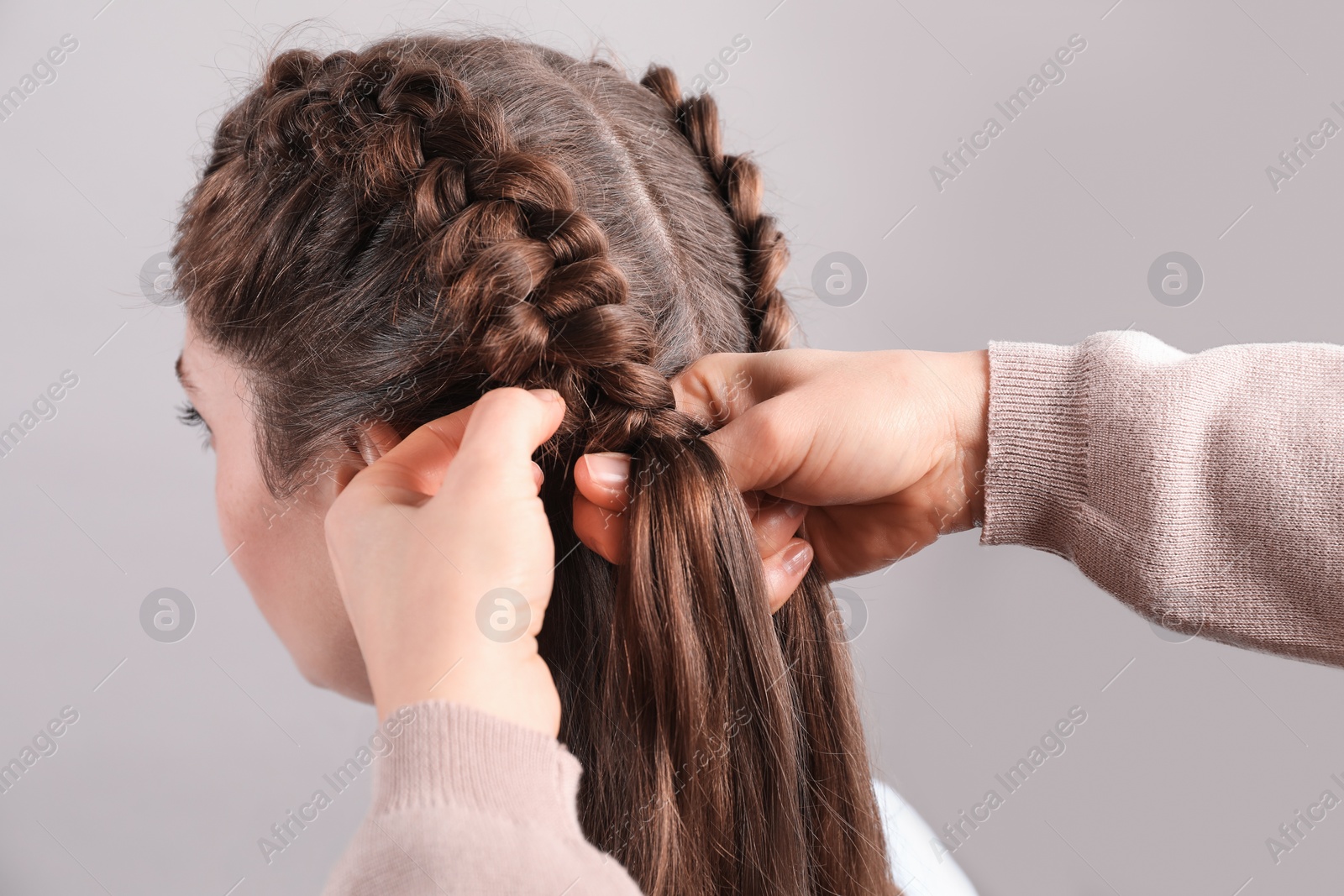 Photo of Professional stylist braiding woman's hair on grey background, closeup