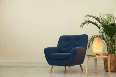 Photo of Stylish room interior with comfortable armchair and plant near beige wall. Space for text