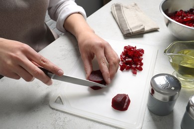 Woman cutting boiled beetroot at white table, closeup. Cooking vinaigrette salad