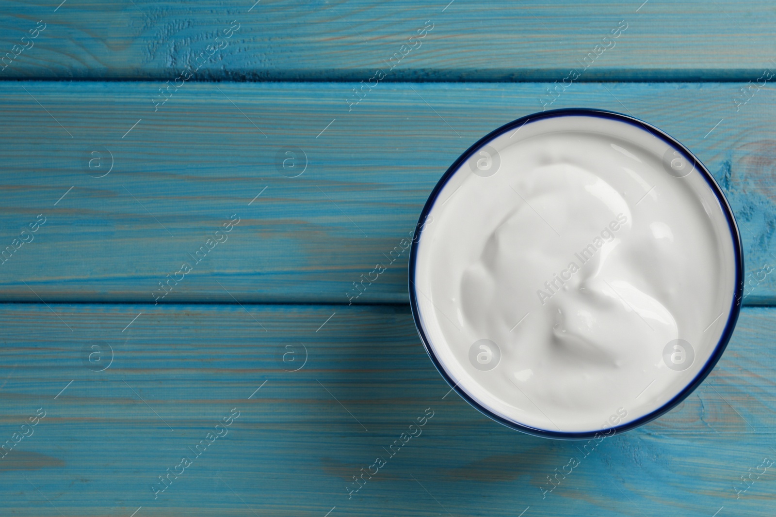 Photo of Bowl of tasty yogurt on light blue wooden table, top view. Space for text