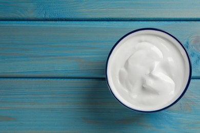 Bowl of tasty yogurt on light blue wooden table, top view. Space for text