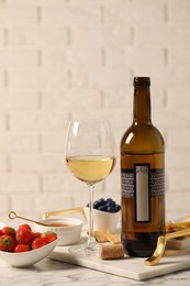 Photo of Bottle of wine, glass and delicious snacks on white marble table