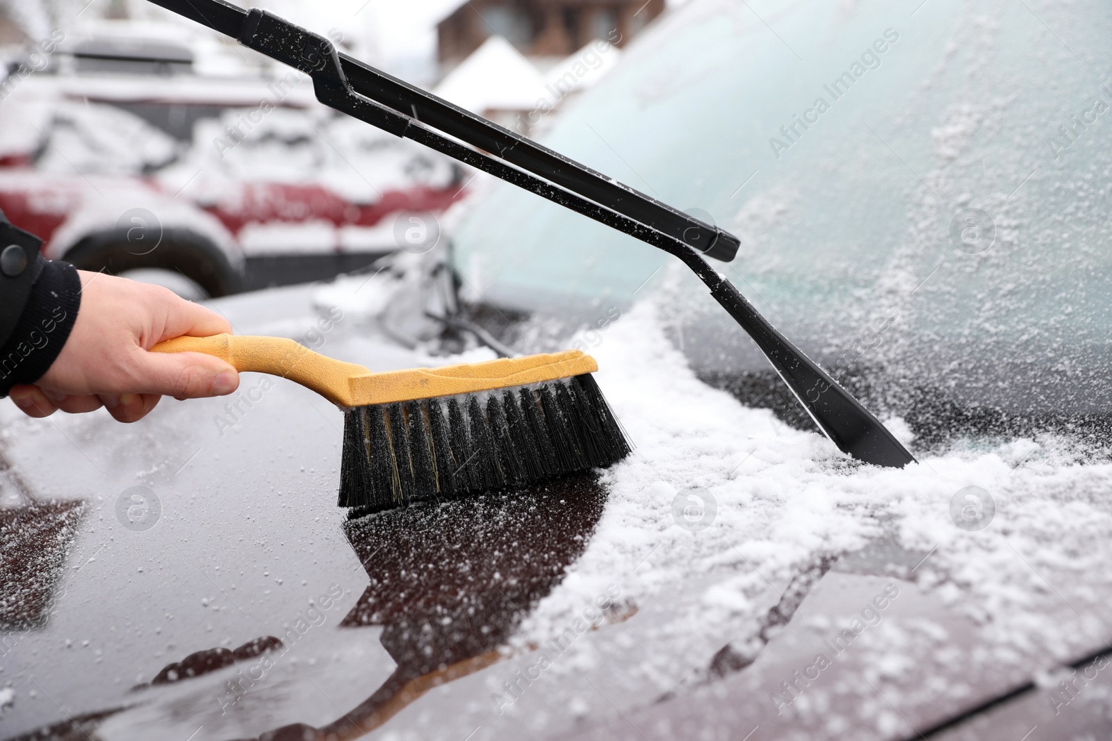 Photo of Man cleaning car hood from snow with brush outdoors, closeup