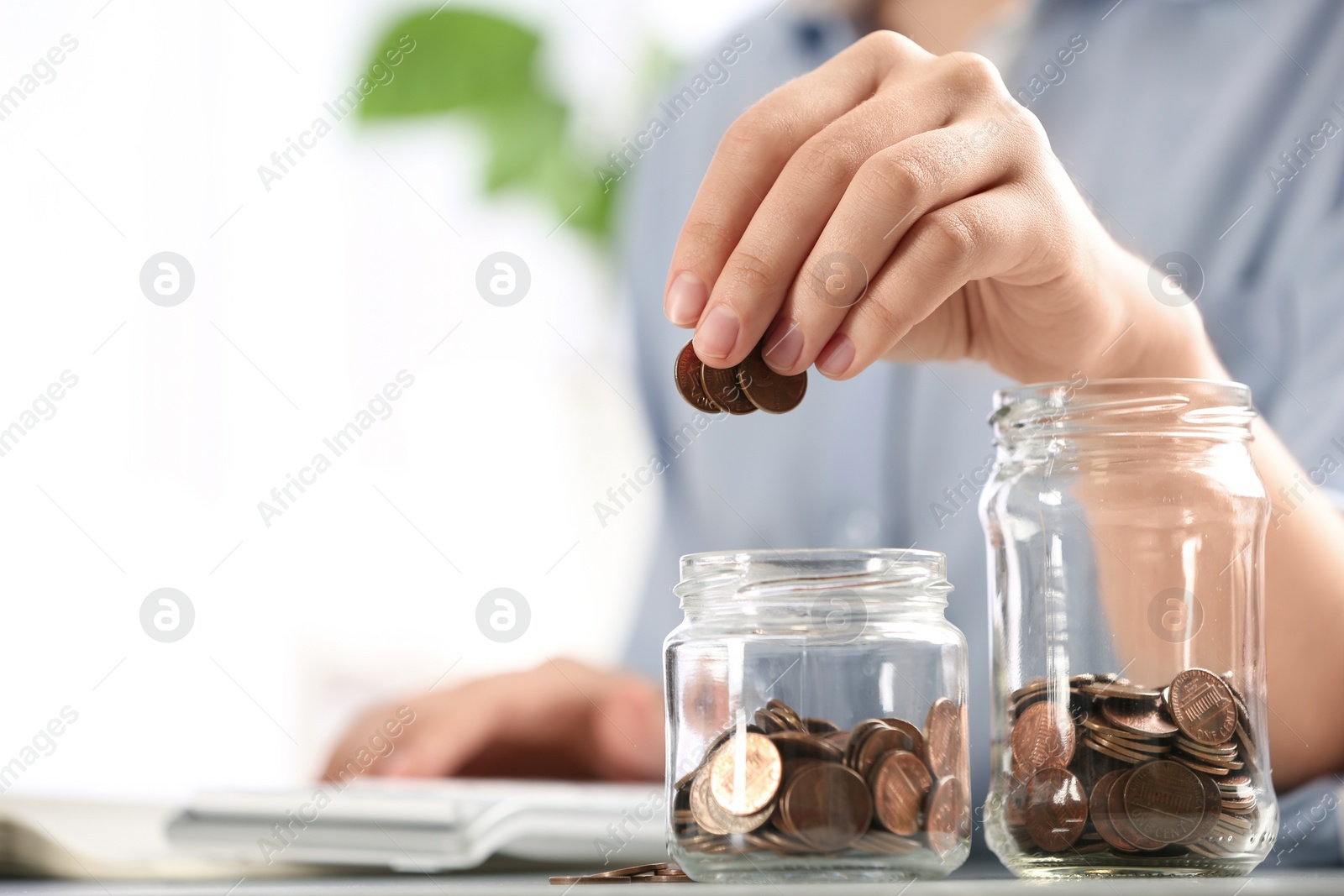 Photo of Woman putting money into glass jar at table, closeup