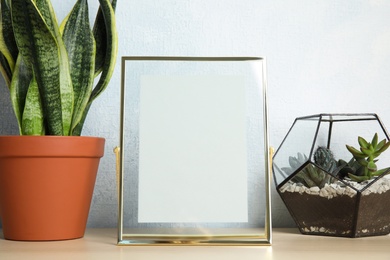 Photo of Exotic plants and photo frame on table near color wall, space for text. Home decor