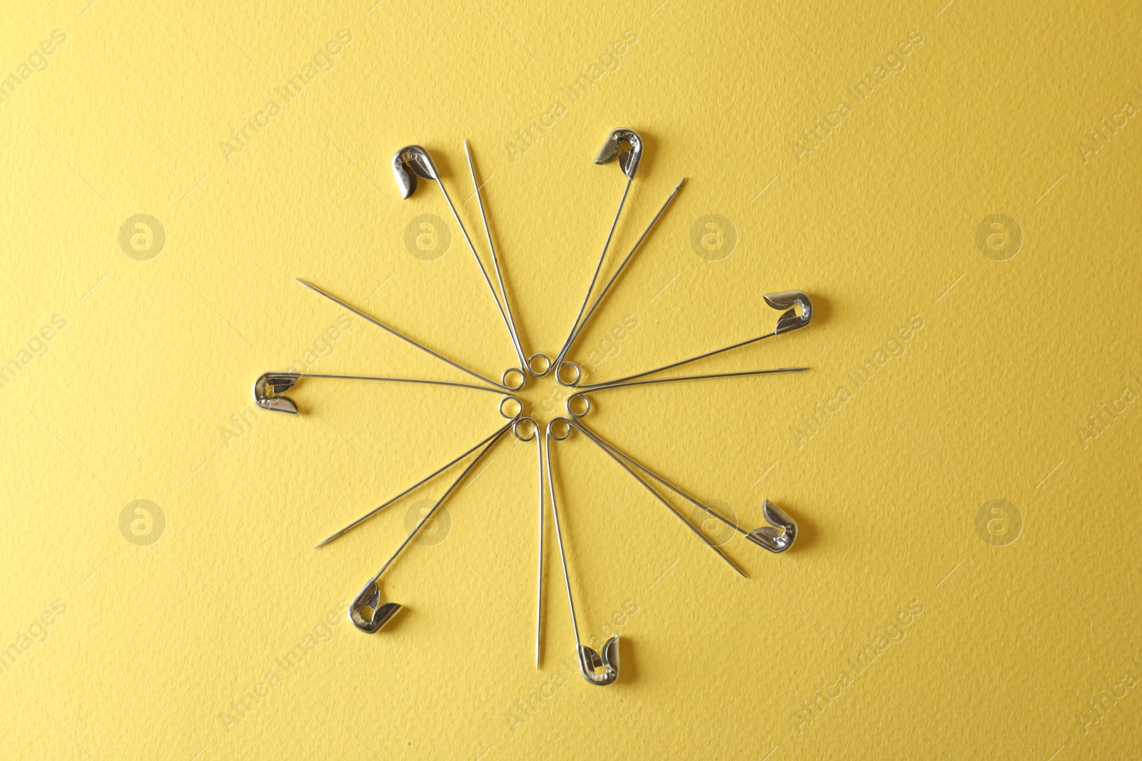 Photo of Safety pins on yellow background, flat lay