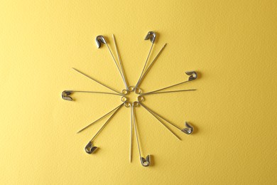 Photo of Safety pins on yellow background, flat lay