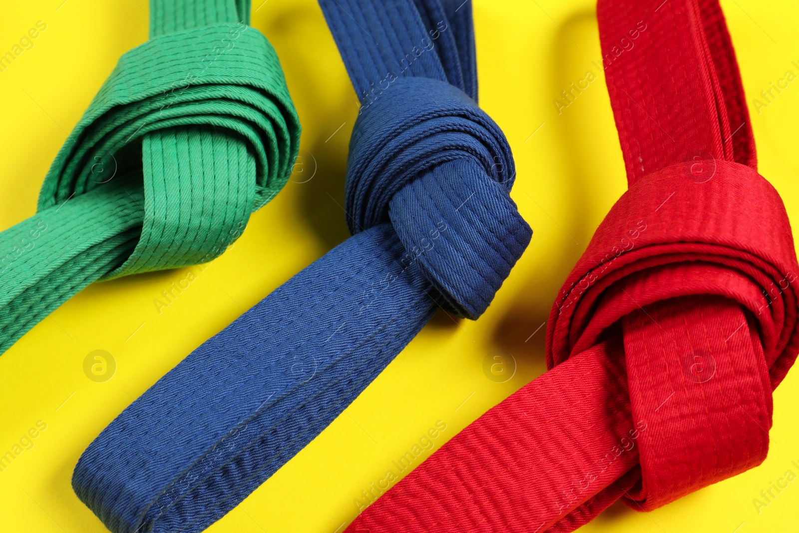 Photo of Colorful karate belts on yellow background, closeup