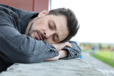 Tired man sleeping on stone parapet outdoors, closeup. Space for text