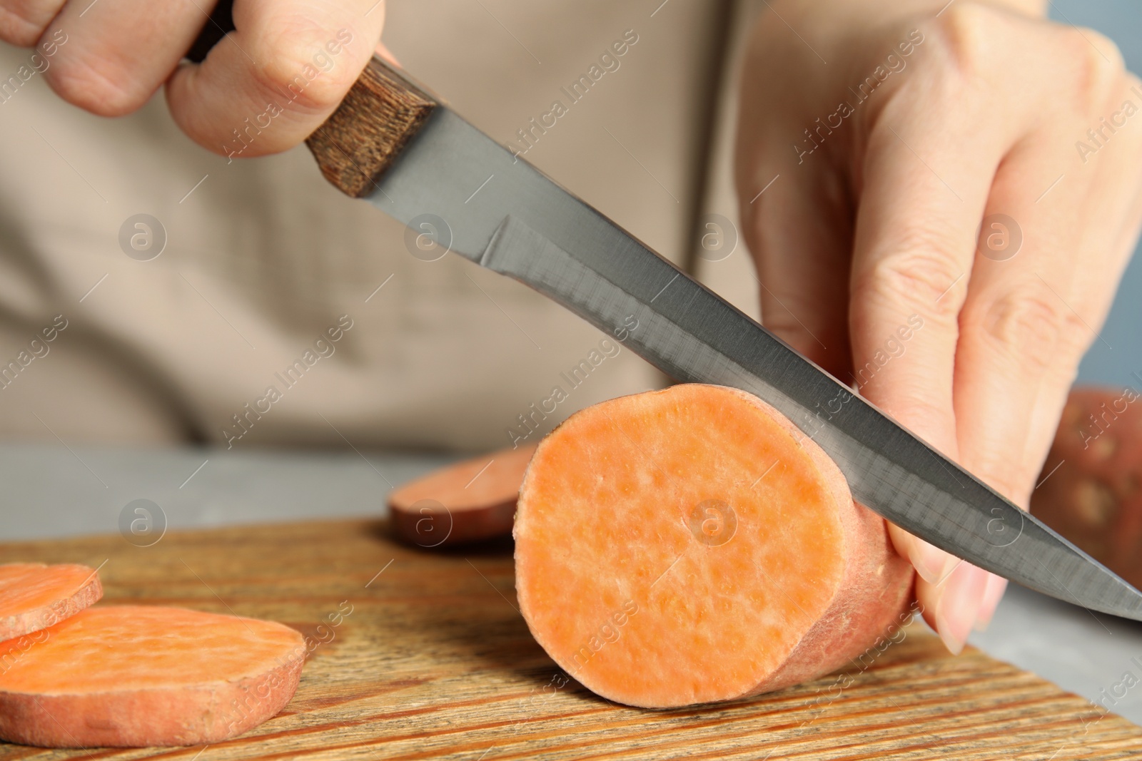 Photo of Woman cutting sweet potato on wooden board, closeup