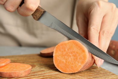 Photo of Woman cutting sweet potato on wooden board, closeup