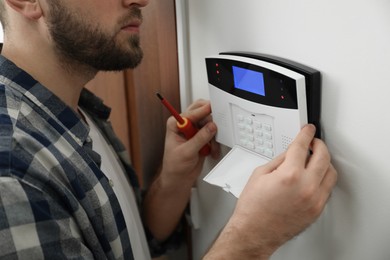 Man installing home security system on white wall in room, closeup