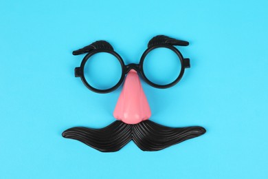 Funny mask with fake mustache, nose and glasses on light blue background, top view