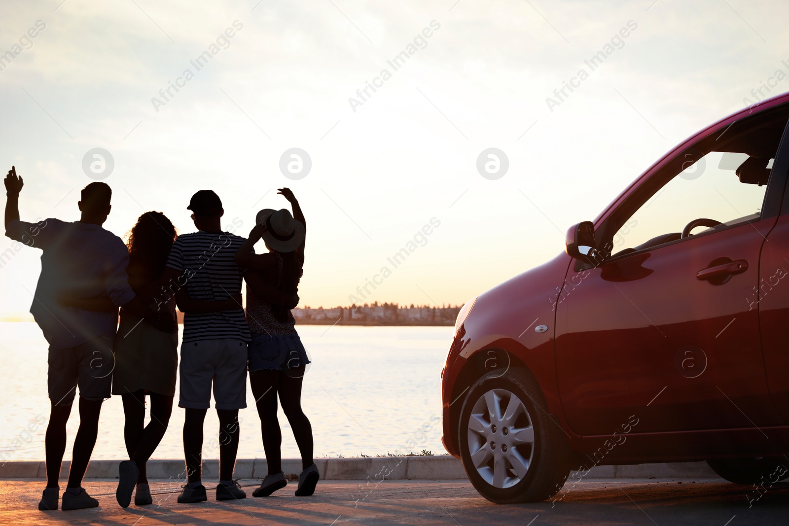 Image of Friends spending time together near car on street, back view. Silhouettes of people at sunset