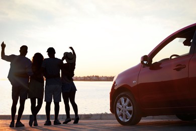 Friends spending time together near car on street, back view. Silhouettes of people at sunset