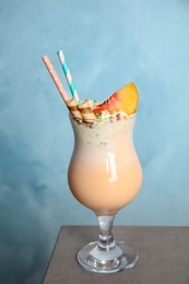 Photo of Glass with delicious milk shake on table against color background