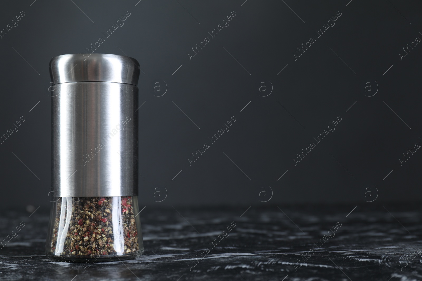 Photo of Pepper shaker on dark marble table, closeup. Space for text