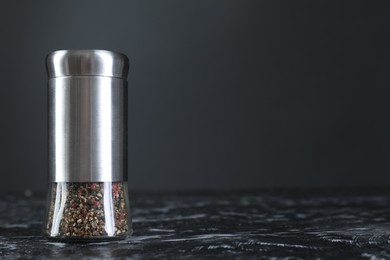 Photo of Pepper shaker on dark marble table, closeup. Space for text