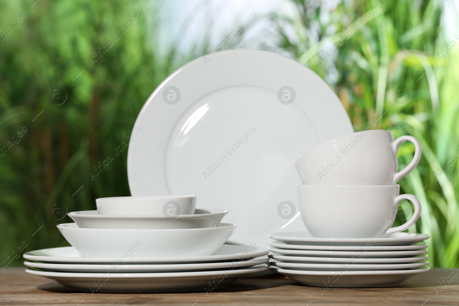 Photo of Set of clean dishware on wooden table against blurred background