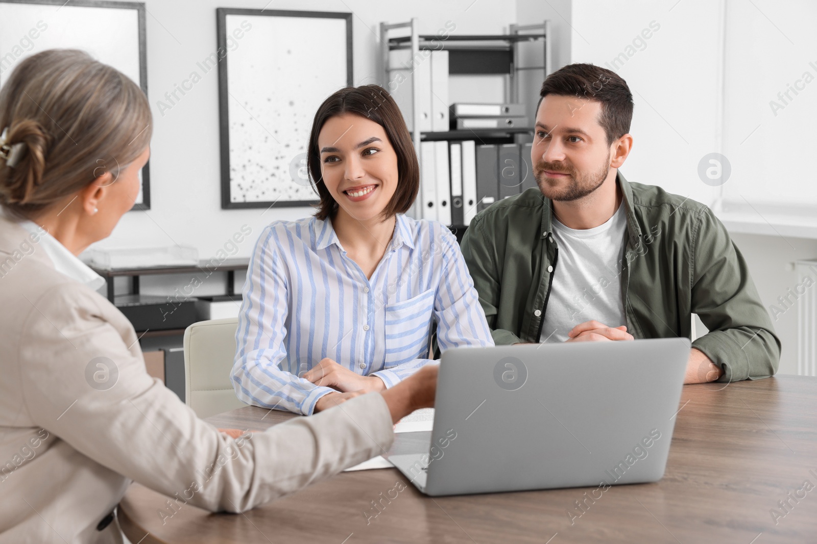 Photo of Young couple consulting insurance agent about pension plan at wooden table indoors