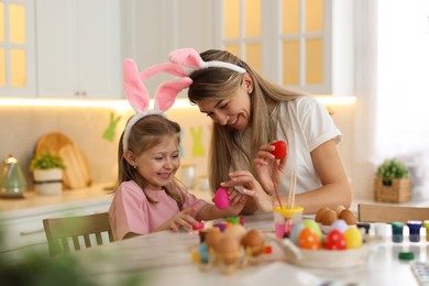 Photo of Easter celebration. Mother with her cute daughter painting eggs at white marble table in kitchen