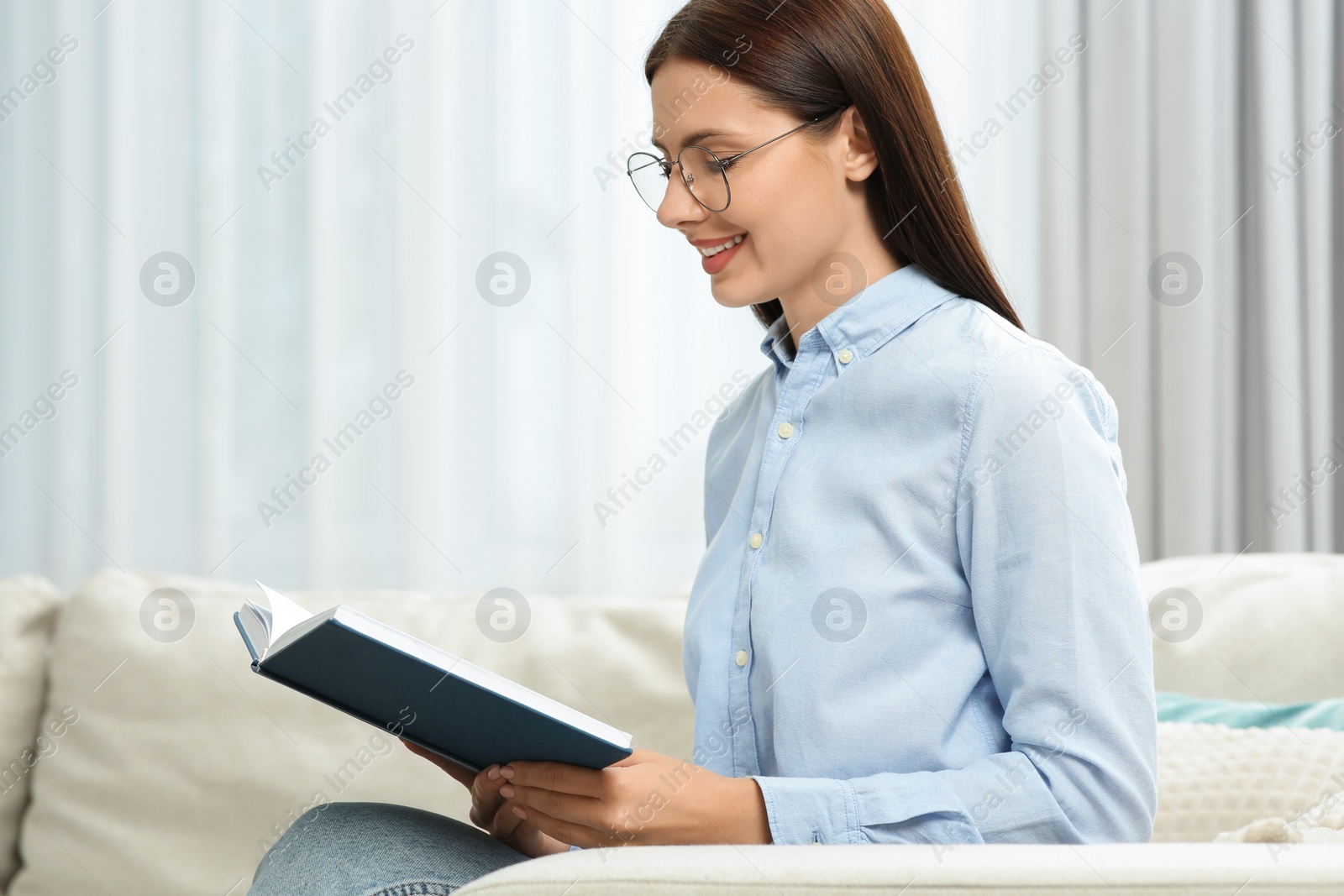 Photo of Smiling woman in stylish eyeglasses reading book at home