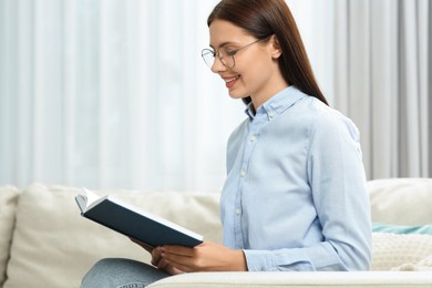 Smiling woman in stylish eyeglasses reading book at home